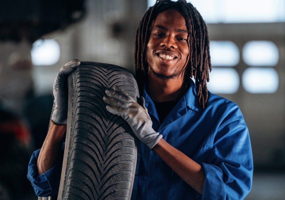 Heavy tire, holding it, changing. Male mechanic is with car in garage.